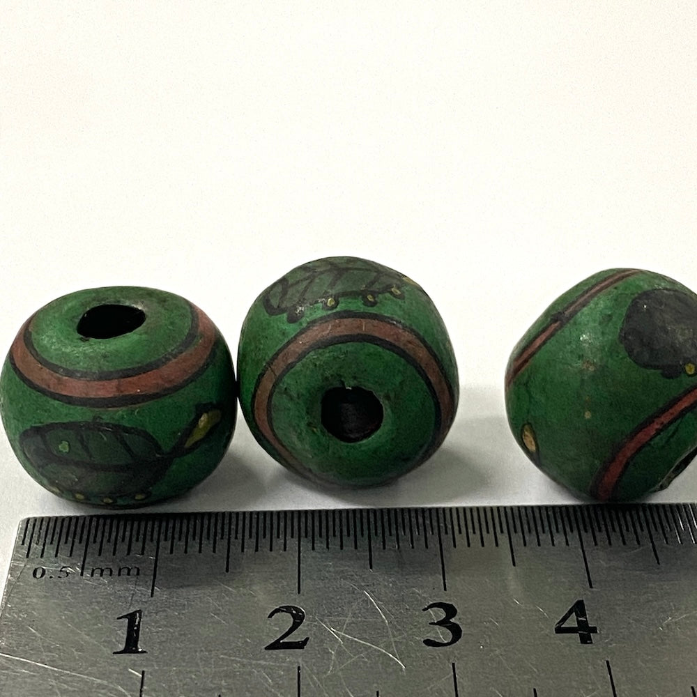 Three green beads with brown accents on a white background, measured against a ruler.
