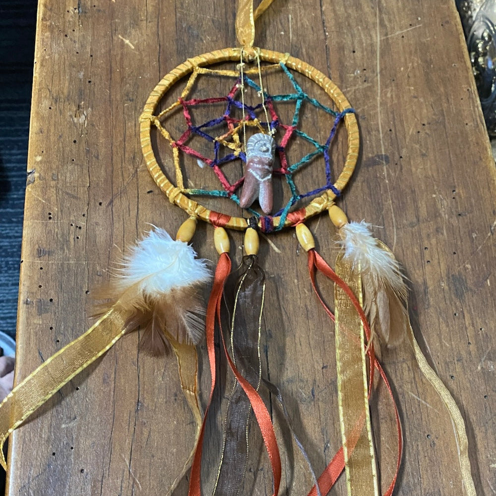 Finished dreamcatcher project on a white background featuring natural brown and gold color cords feathers and beads and a centre feature of a Peru handmade ceramic clay Pachamama doll made for a new baby nursery room as a gift