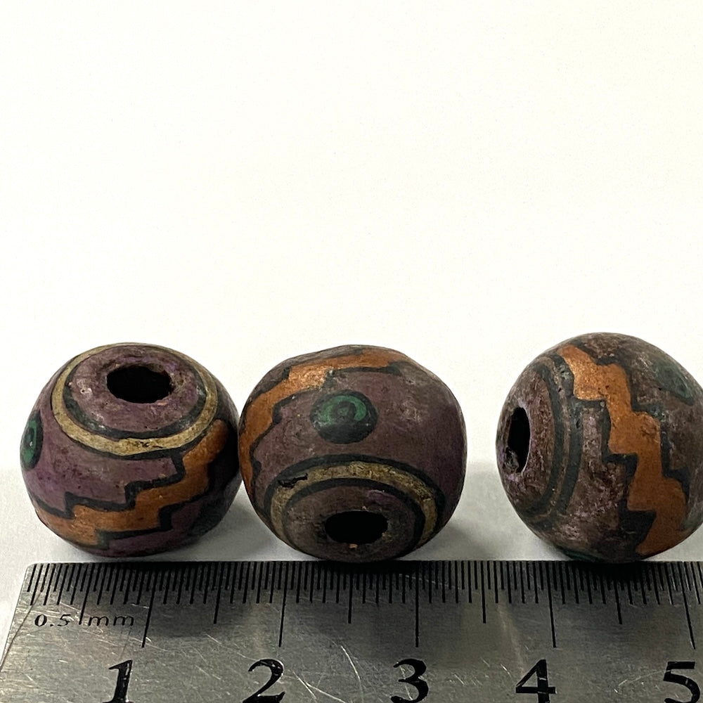 Three decorative beads with intricate patterns on a white background, accompanied by a ruler for scale.