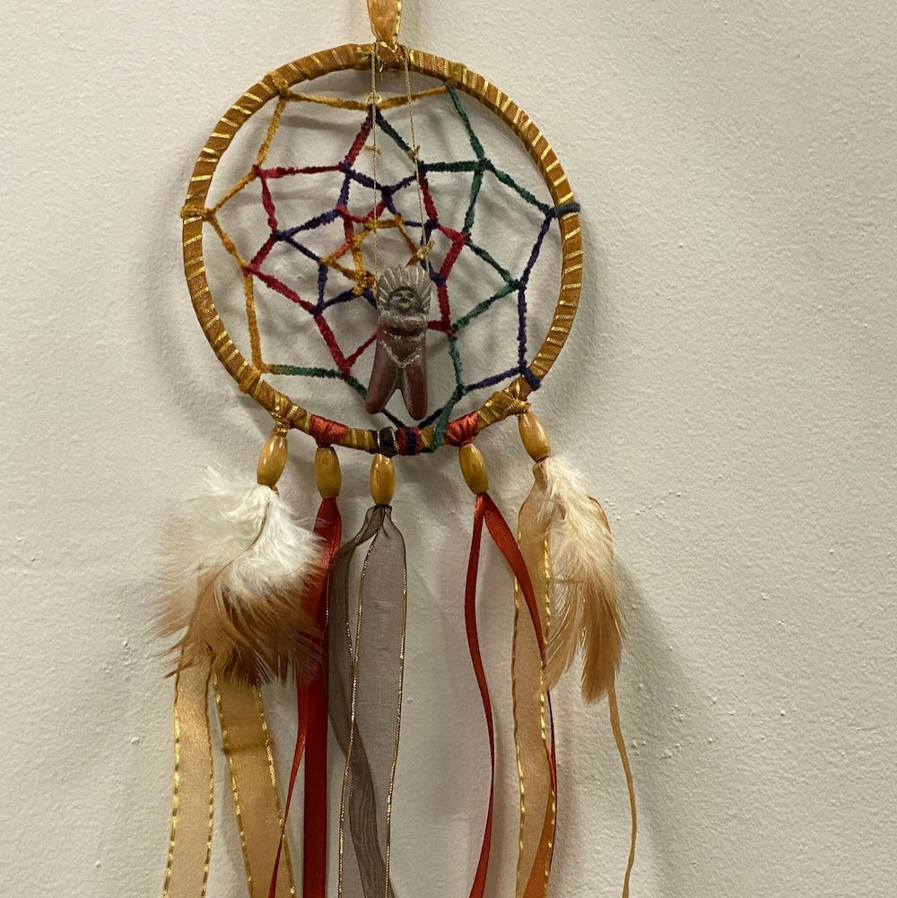 Finished dreamcatcher project on a white background featuring natural brown and gold color cords feathers and beads and a centre feature of a Peru handmade ceramic clay Pachamama doll made for a new baby nursery room as a gift