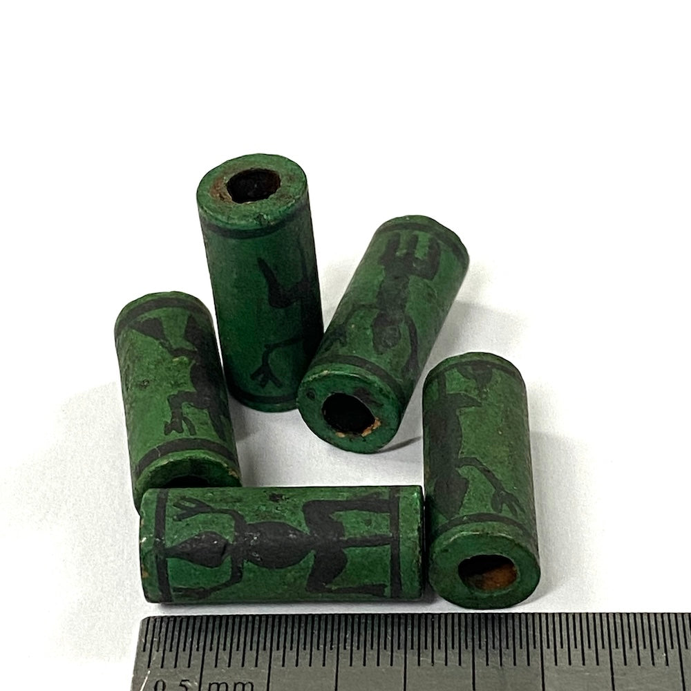 Green cylindrical vintage ceramic beads with black designs on a white background, accompanied by a ruler for scale.