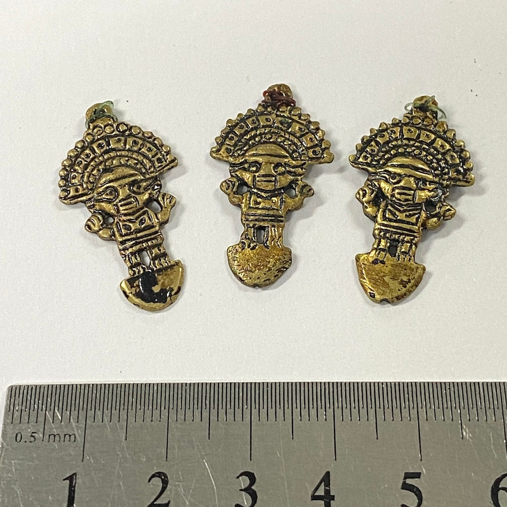 Three metallic figurines with headdresses on a white background, with a ruler for scale.