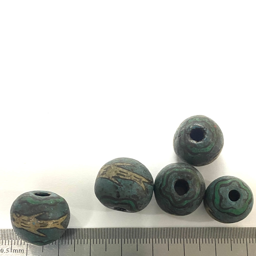 Five antique beads with textured surface and central hole on a white background, with a ruler for scale.