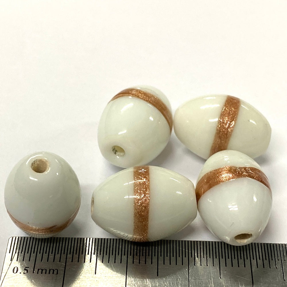 White beads with gold stripes on a white background with a ruler for scale.