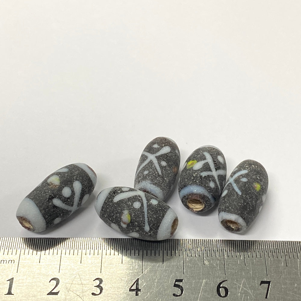 Set of six gray beads with white and yellow patterns on a white background, with a ruler for scale.