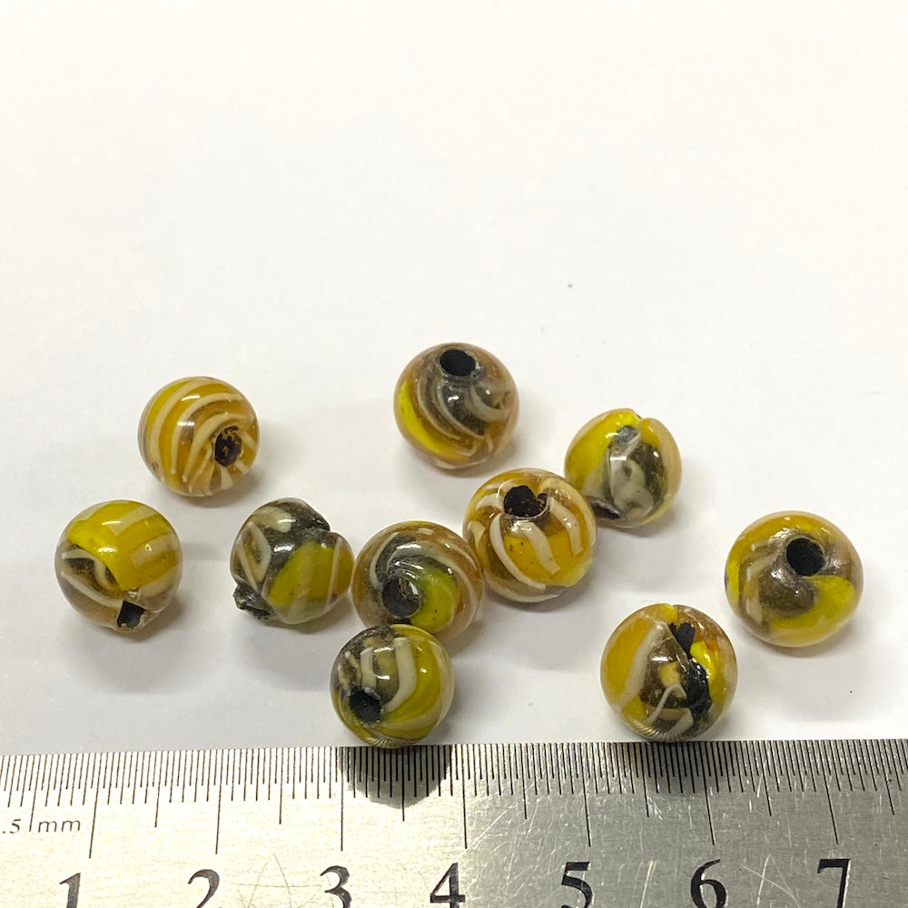 Yellow and black marbled beads with a ruler for scale on a white background