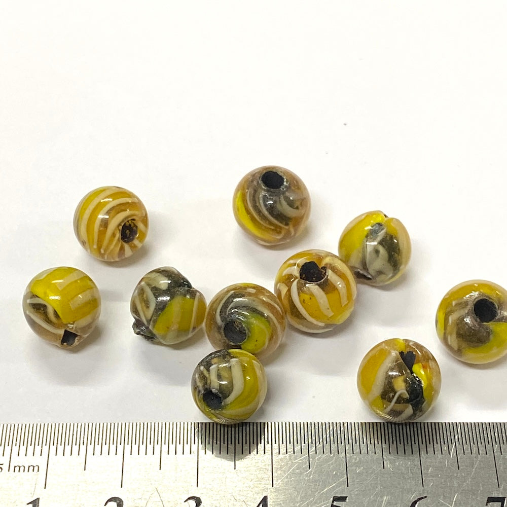 Yellow and black marbled beads with a ruler for scale on a white background