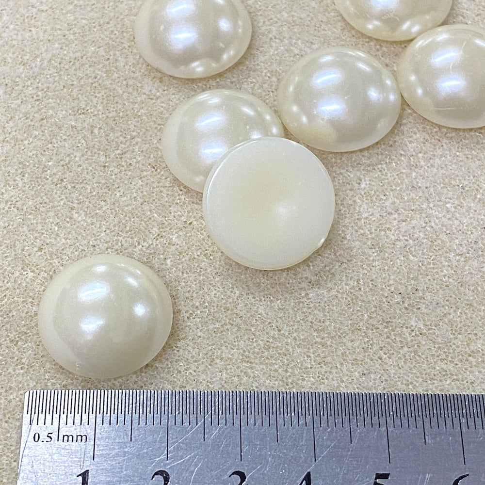 White pearl cabochons on a textured surface with a ruler for scale.