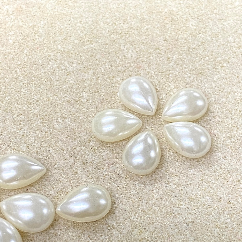 Pearl teardrop-shaped stones on a beige sand background
