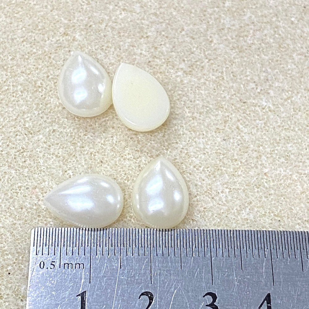 Four teardrop-shaped pearls on a textured surface with a ruler for scale.
