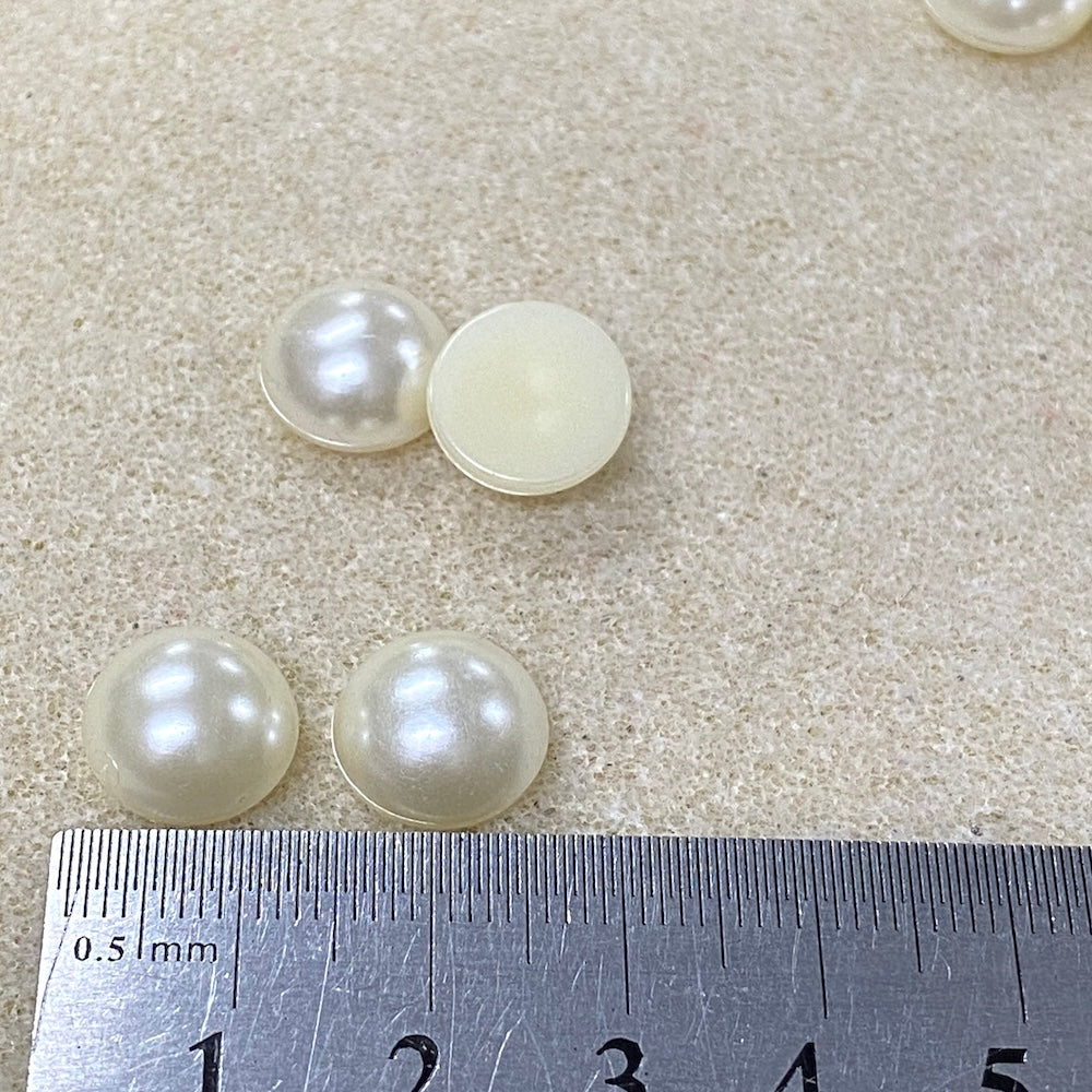 Four pearls on a light beige surface with a ruler for scale.