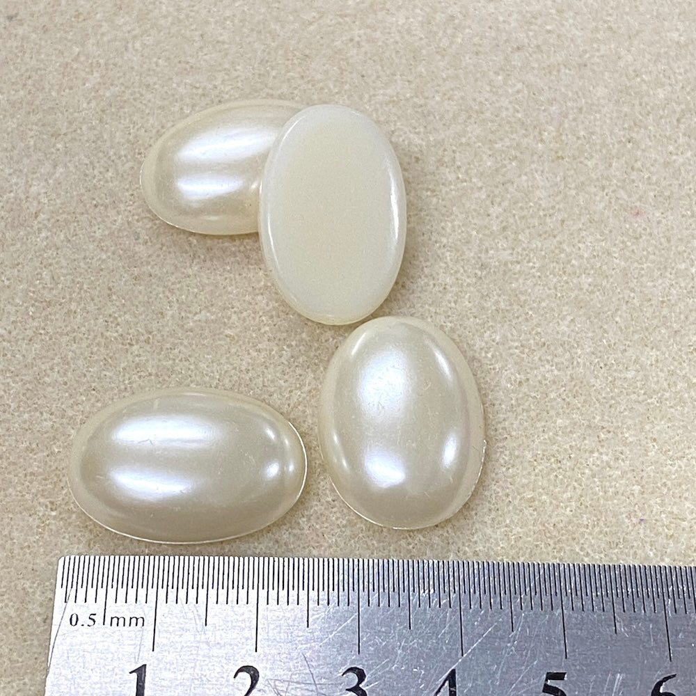 Four oval-shaped pearl cabochons on a textured surface with a ruler for scale.