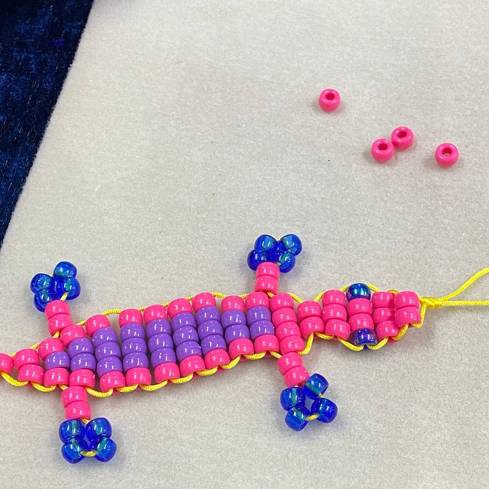A gecko beaded kit showing beads in blue pink and purple on a cream background