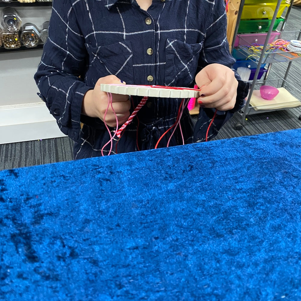 girls hands working on a Kumihimo weaving project key ring at Bead Shack workshop table showing a blue background