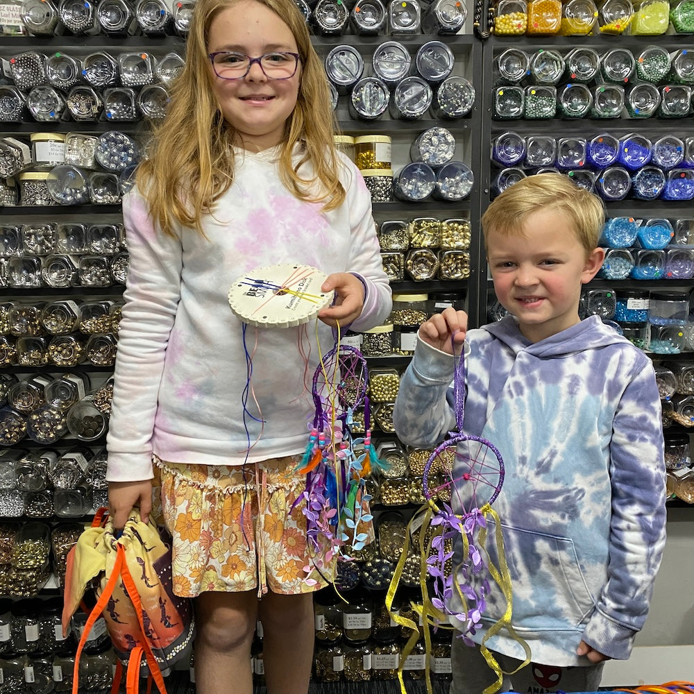 Two children holding up craft activities completed from their workshop. Dreamcatchers and Kumihimo braid