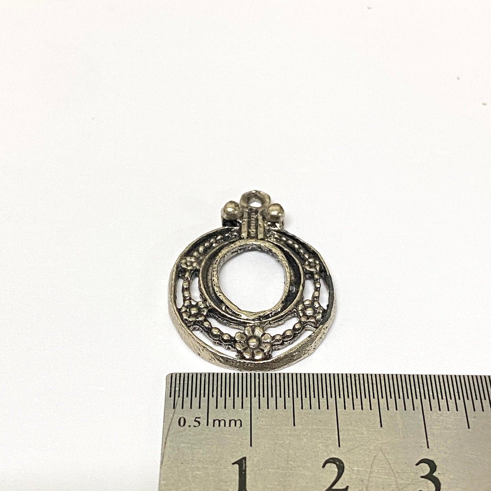 Decorative silver pendant with a ruler for scale on a white background