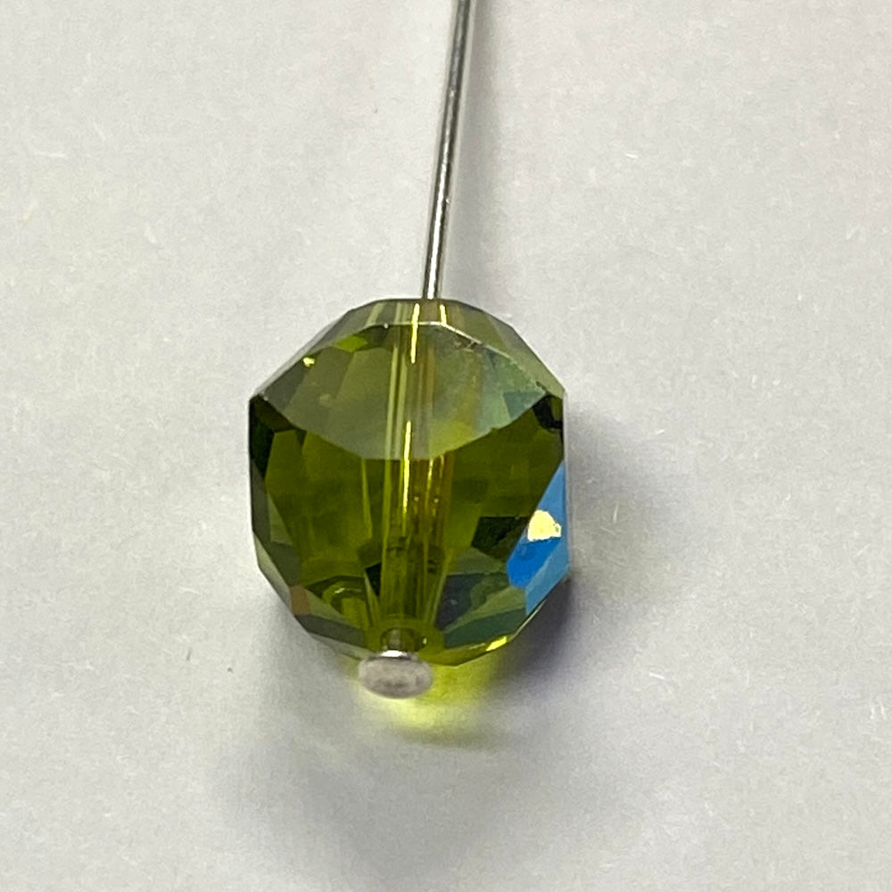 Green faceted crystal bead held by a pin on a white background