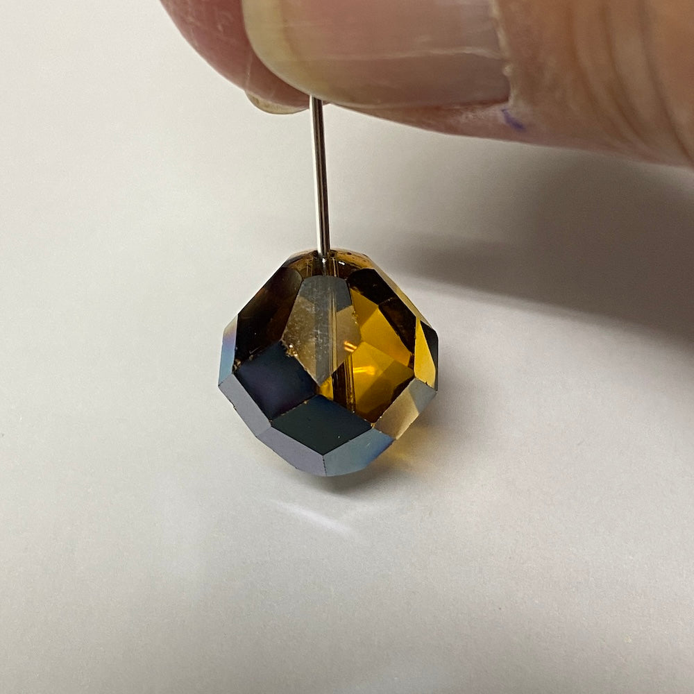 Faceted brown crystal bead held by pin on a white background