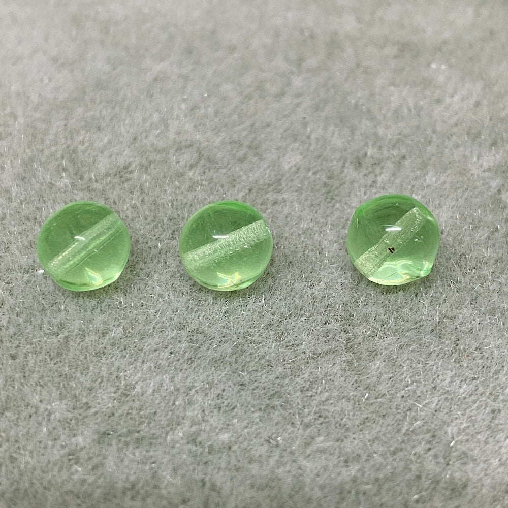 Three green vaseline glass vintage beads on a gray surface