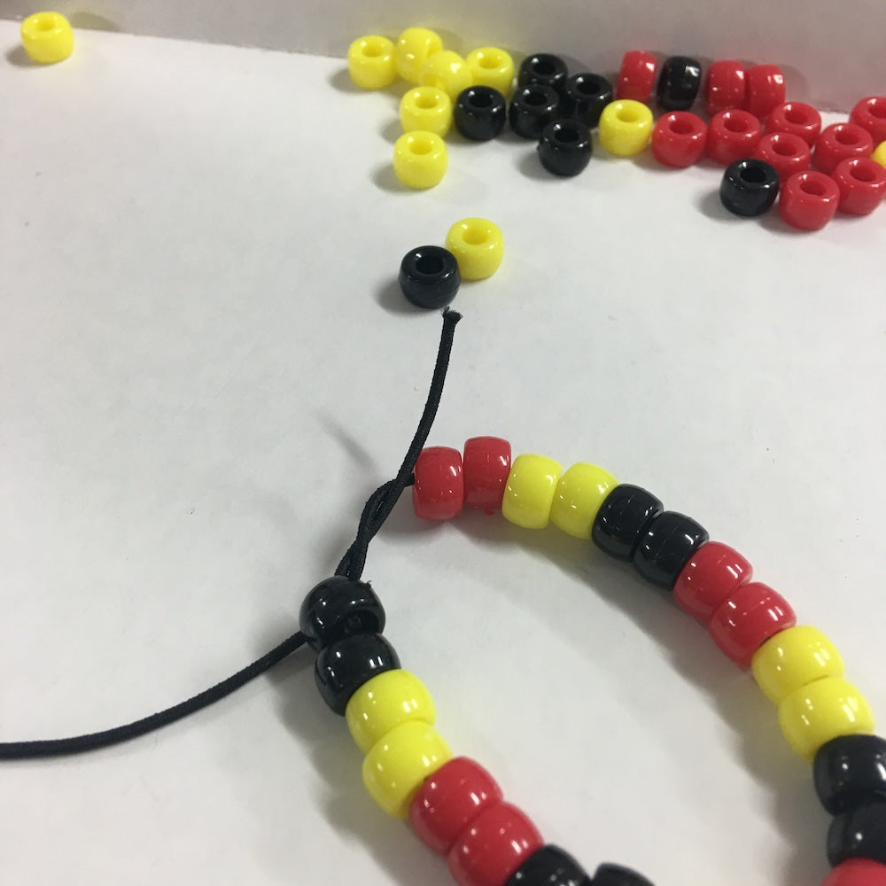 Beaded tribal bracelet with red, yellow, and black pony beads on black elastic on a white background