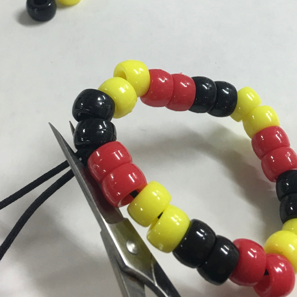 Colorful beaded bracelet with scissors cutting through it on a white background