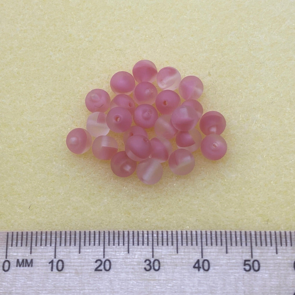 Strawberry pink and transparent beads in a group on a cream background with a ruler to show scale
