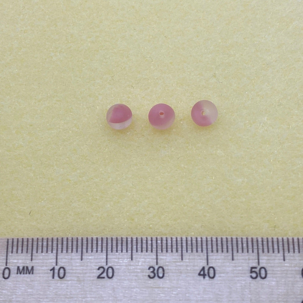 3 Strawberry pink and transparent beads in a group on a cream background with a ruler to show scale