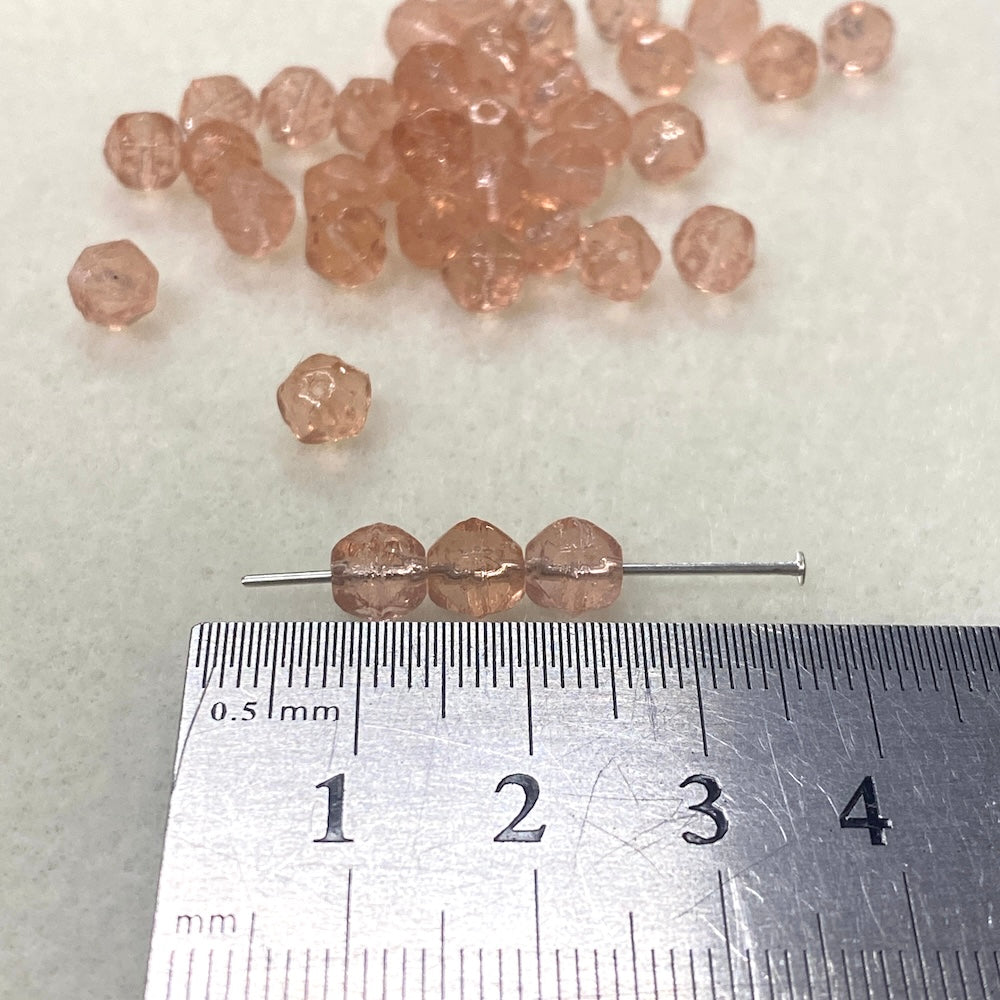 Small pink beads on a white background with a ruler for scale.