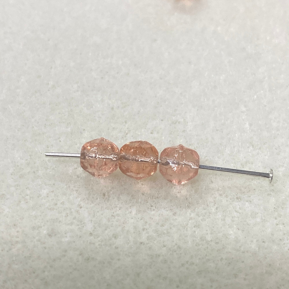 Three pink beads on a needle against a light gray background
