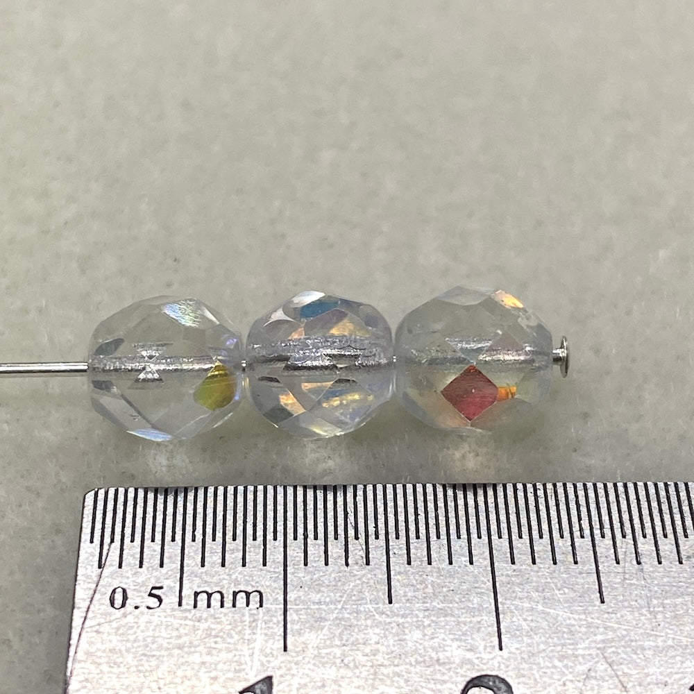 Three clear beads on a needle with a ruler for scale on a gray background
