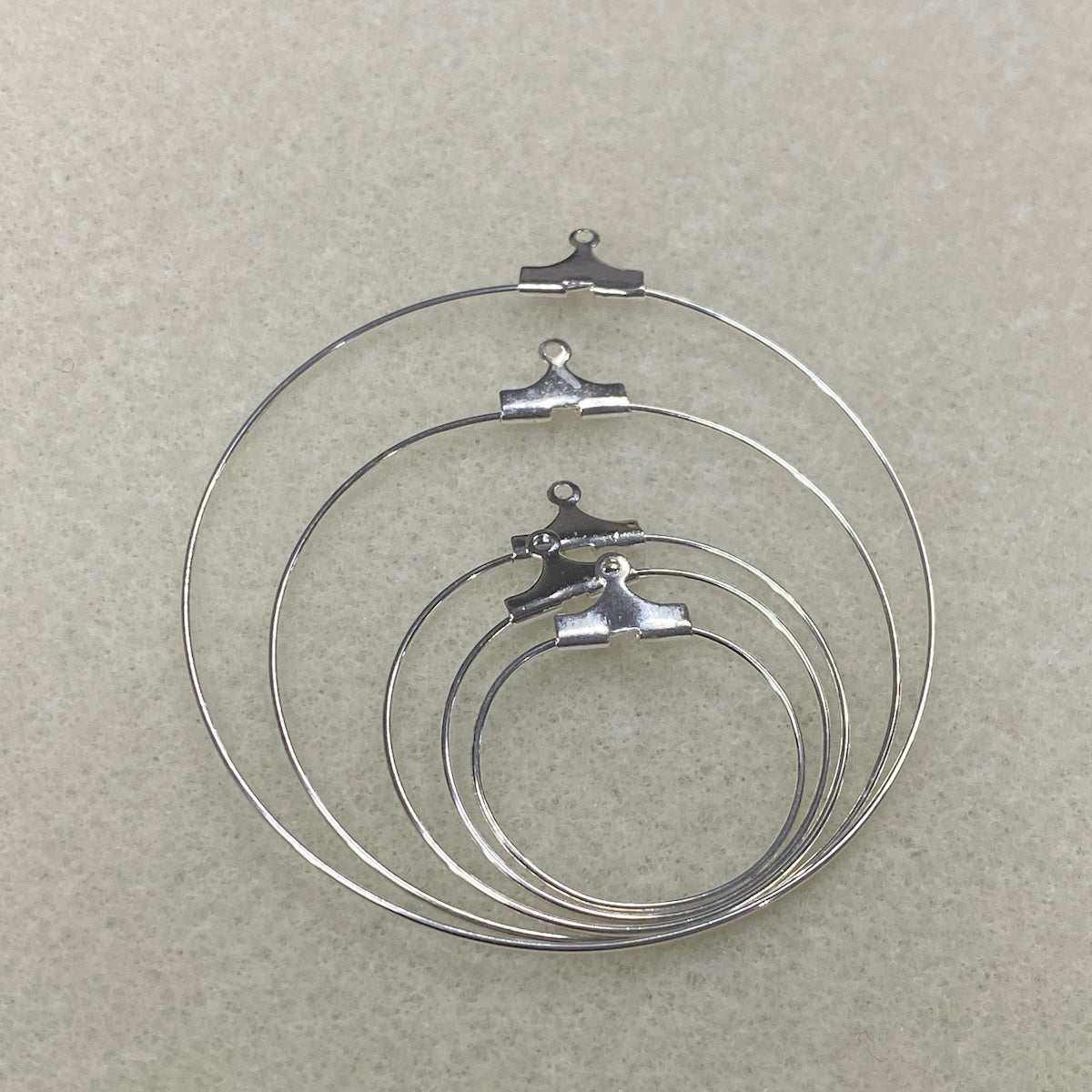 Set of five graded sized metal ear hoop earring fittings with clips on a gray background