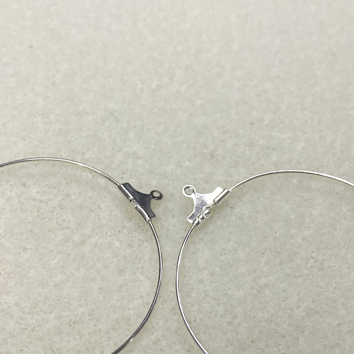 Two metal eye ear circle hoops on a beige background