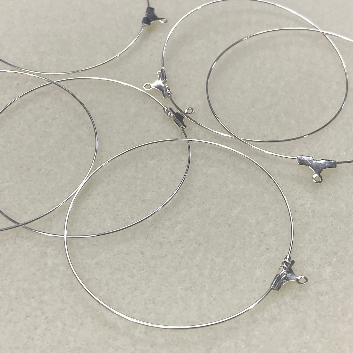 Silver wire ear loop fittings with clasp ends on a beige background