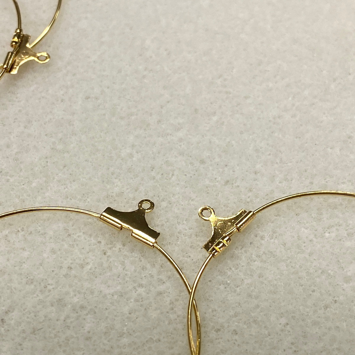 Gold hoop earrings with clasp mechanism on a light gray background