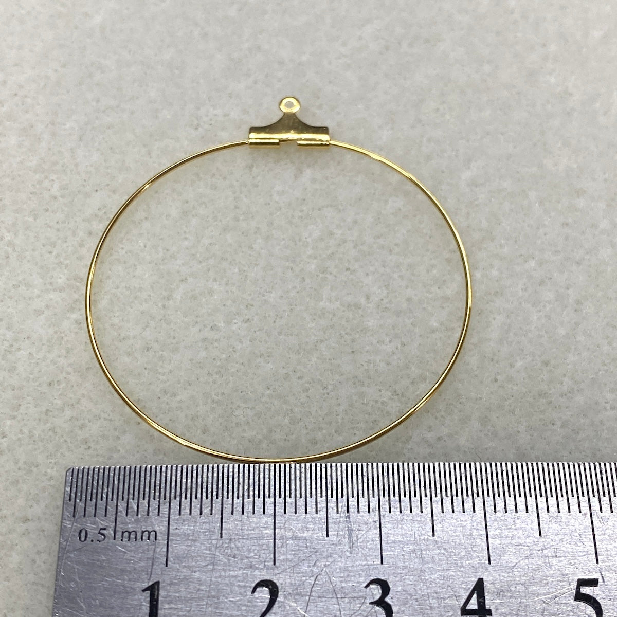Gold ear loop fitting on a light gray background with a ruler for scale.