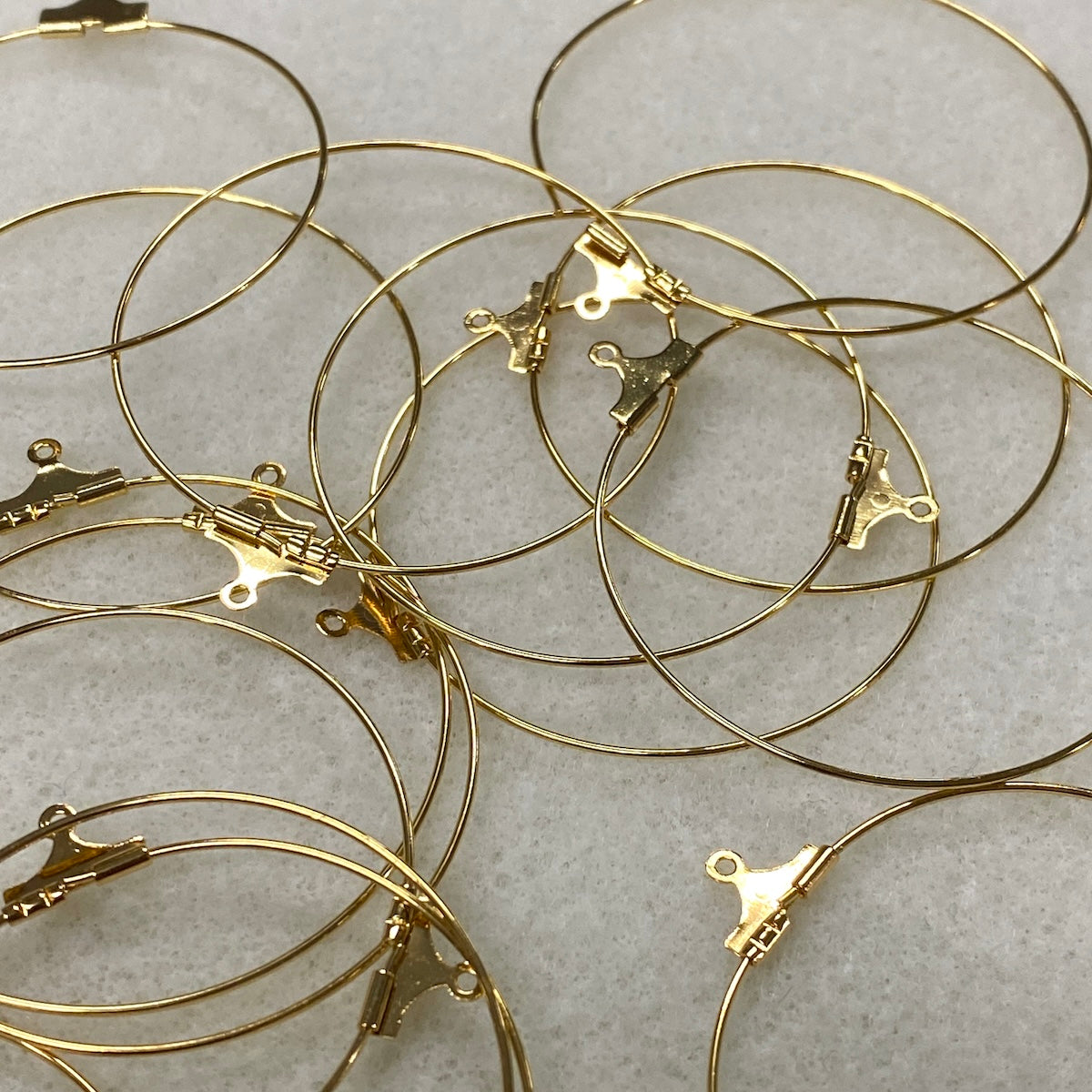 Gold hoop earrings with clasp mechanisms on a light gray background