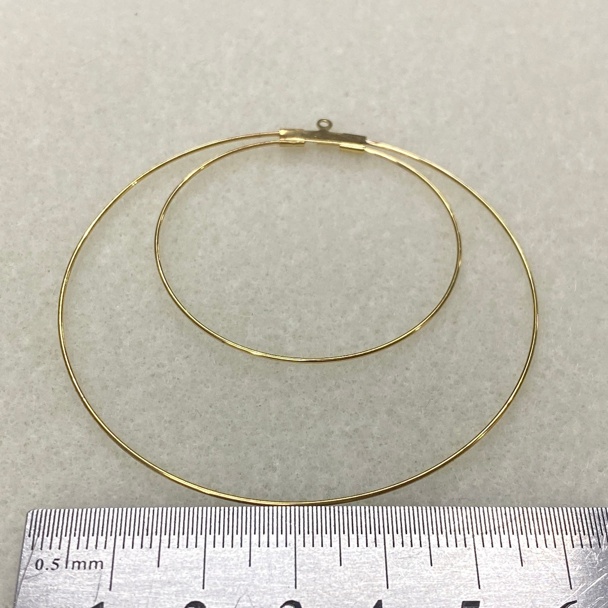 Gold hoop earring on a light gray background with a ruler for scale.