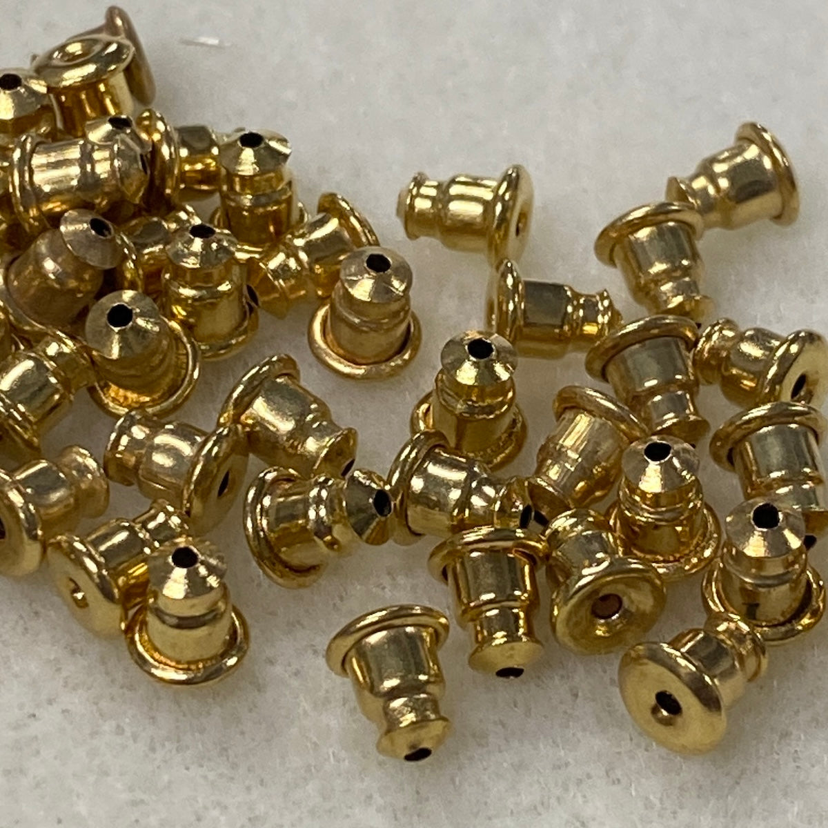 Gold metal bullet backs for ear studs on a light gray background