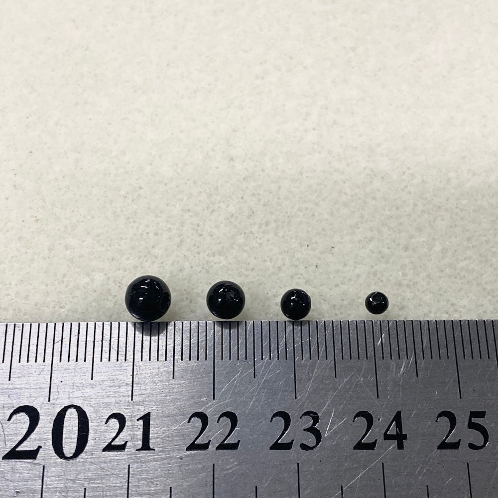 Four black beads on a ruler for size reference against a white background