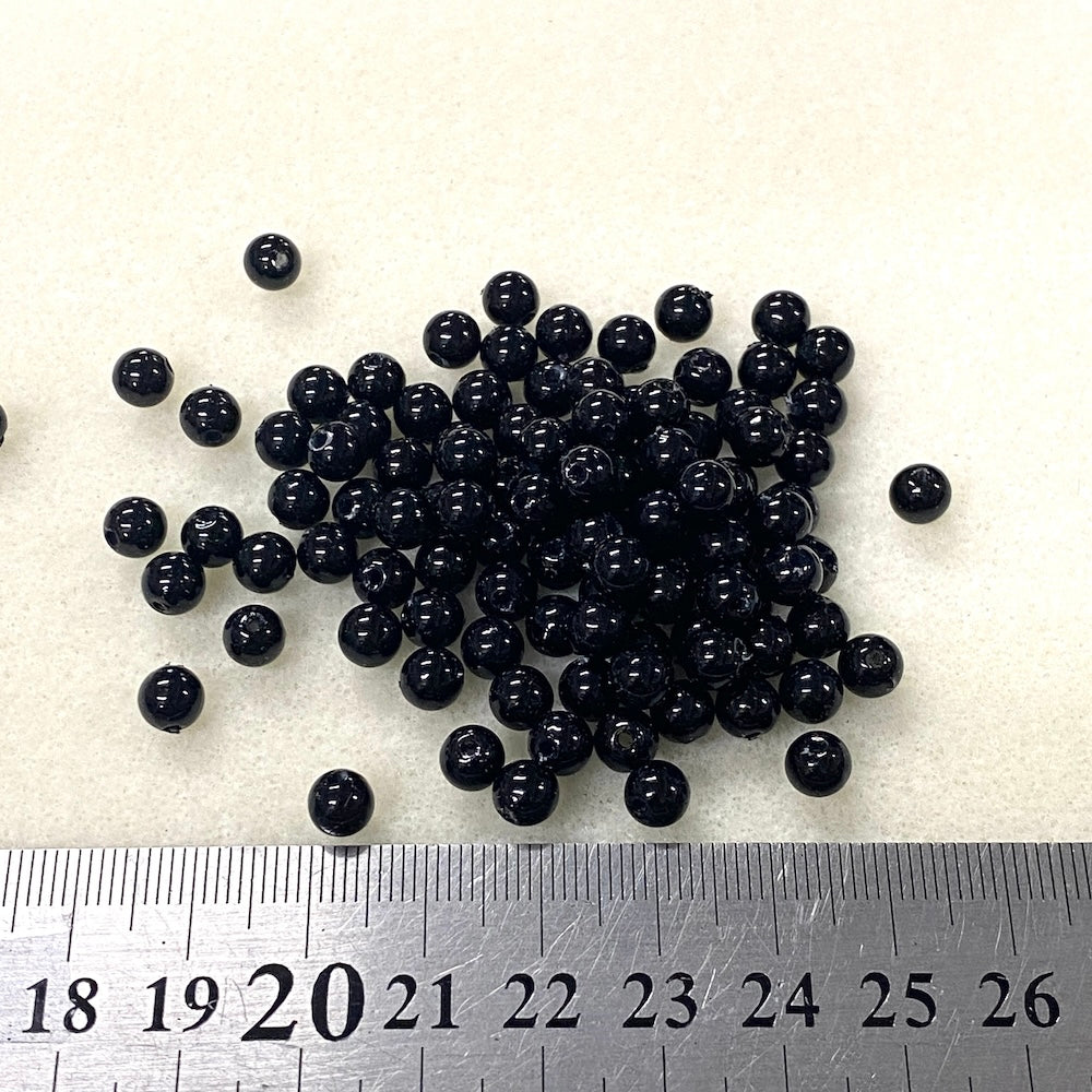 Black beads on a white background with a ruler for scale.