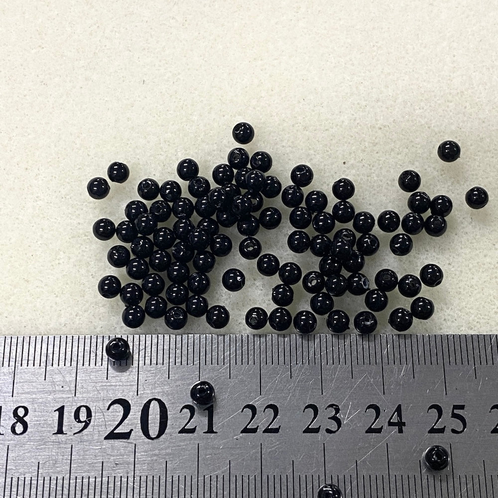 Black beads on a white background with a ruler for scale