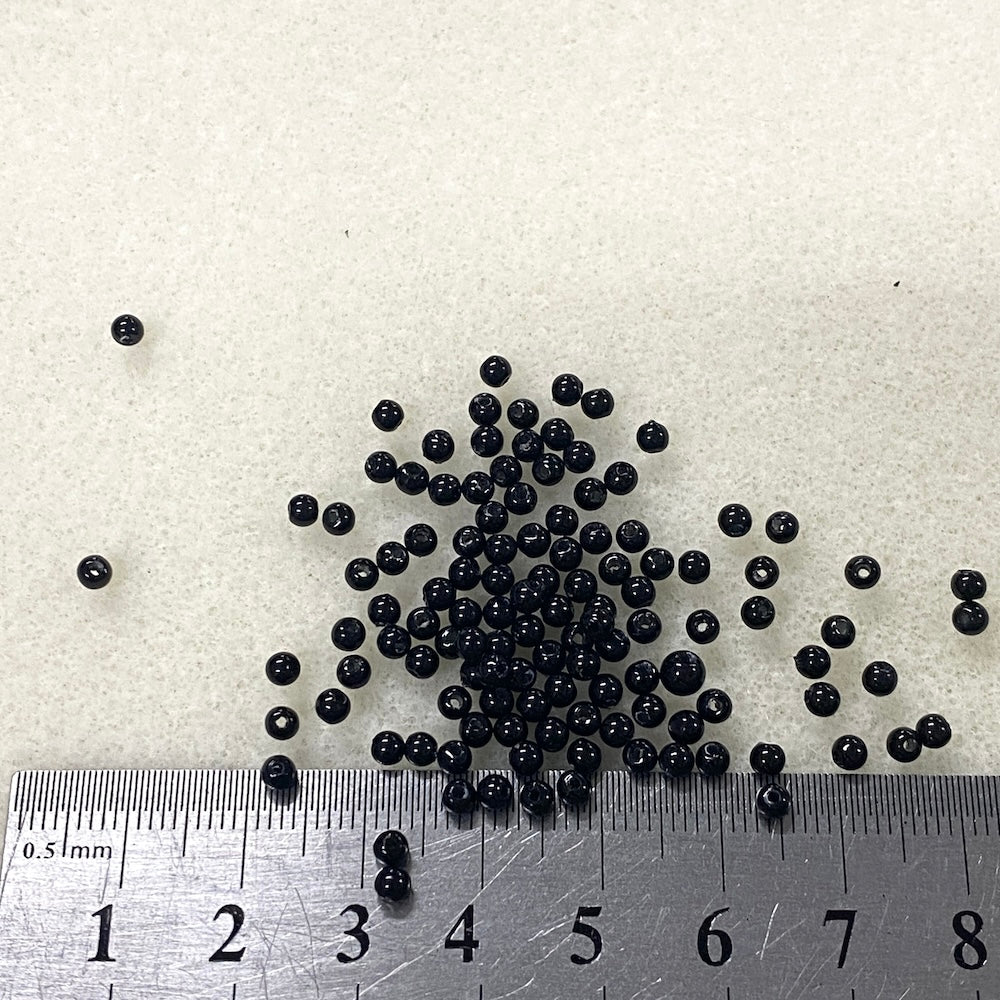 Small black beads on a white background with a ruler for scale.