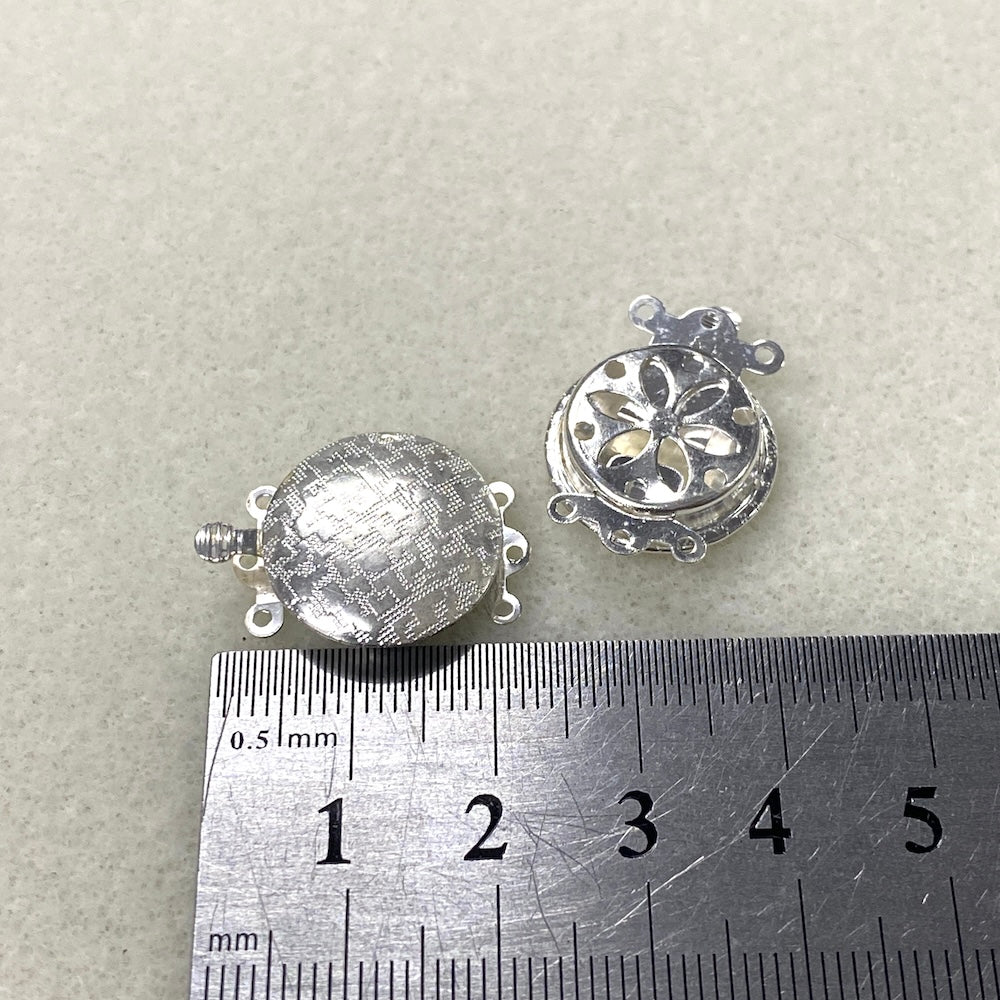 Two silver jewelry components on a gray background with a ruler for scale.