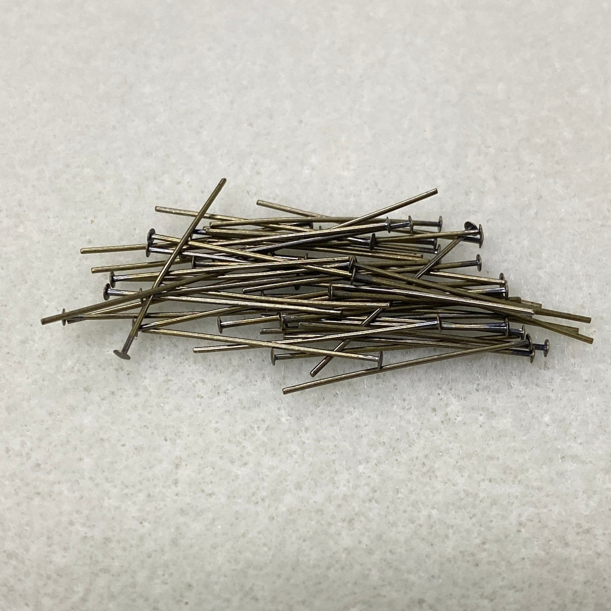 Pile of metal jewelry making pins on a textured white surface