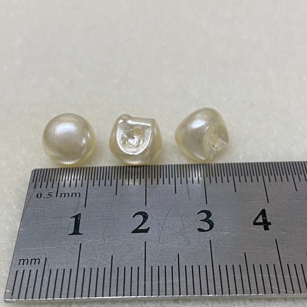 Three pearl buttons next to a ruler on a light gray background