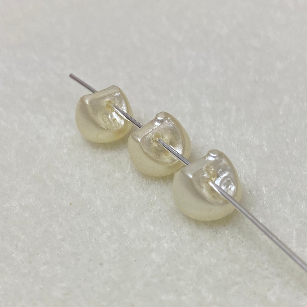 Three pearl buttons on a needle against a textured white background