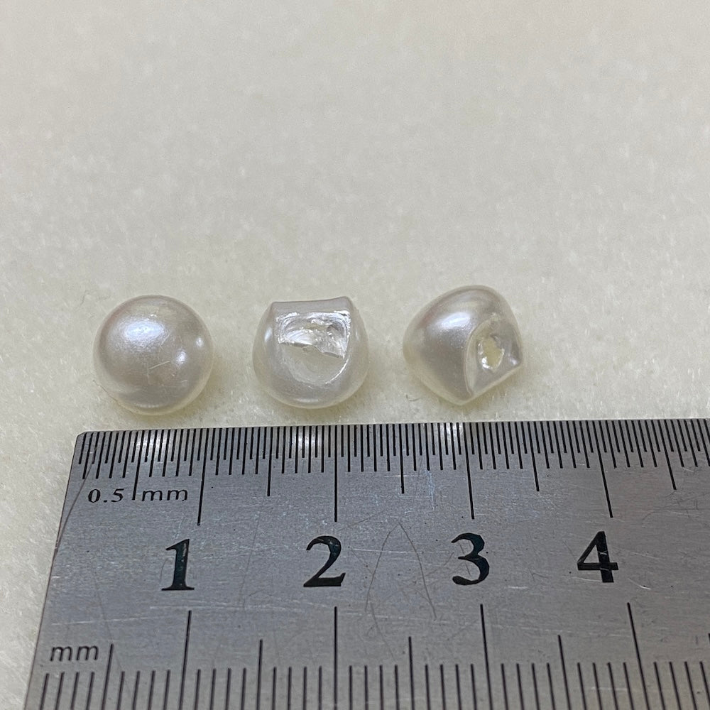 Three pearl buttons on a ruler for size reference