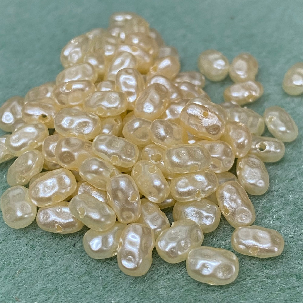 A pile of flat, cream-colored acrylic pearls with a rice bubble-like appearance, intended for crafting and jewelry making.