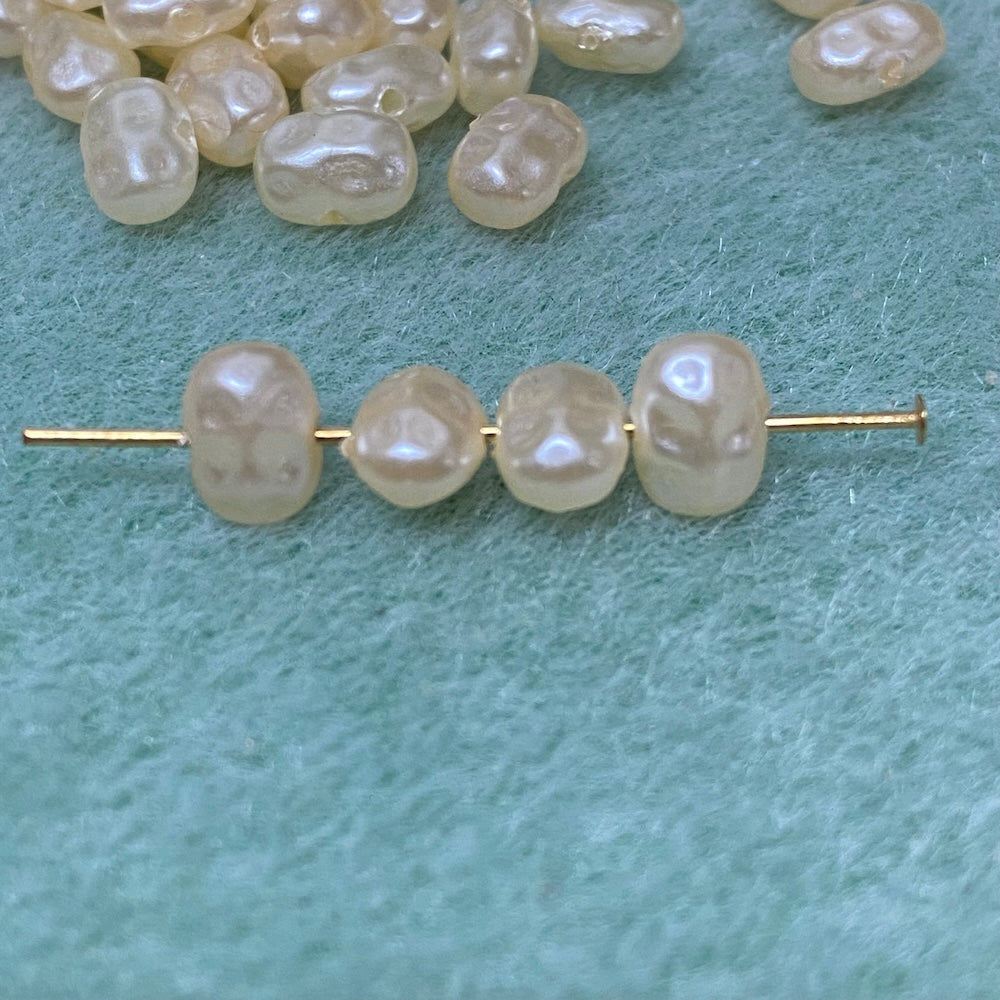 Flat pearls in cream on a pin showing where the holes in the beads are