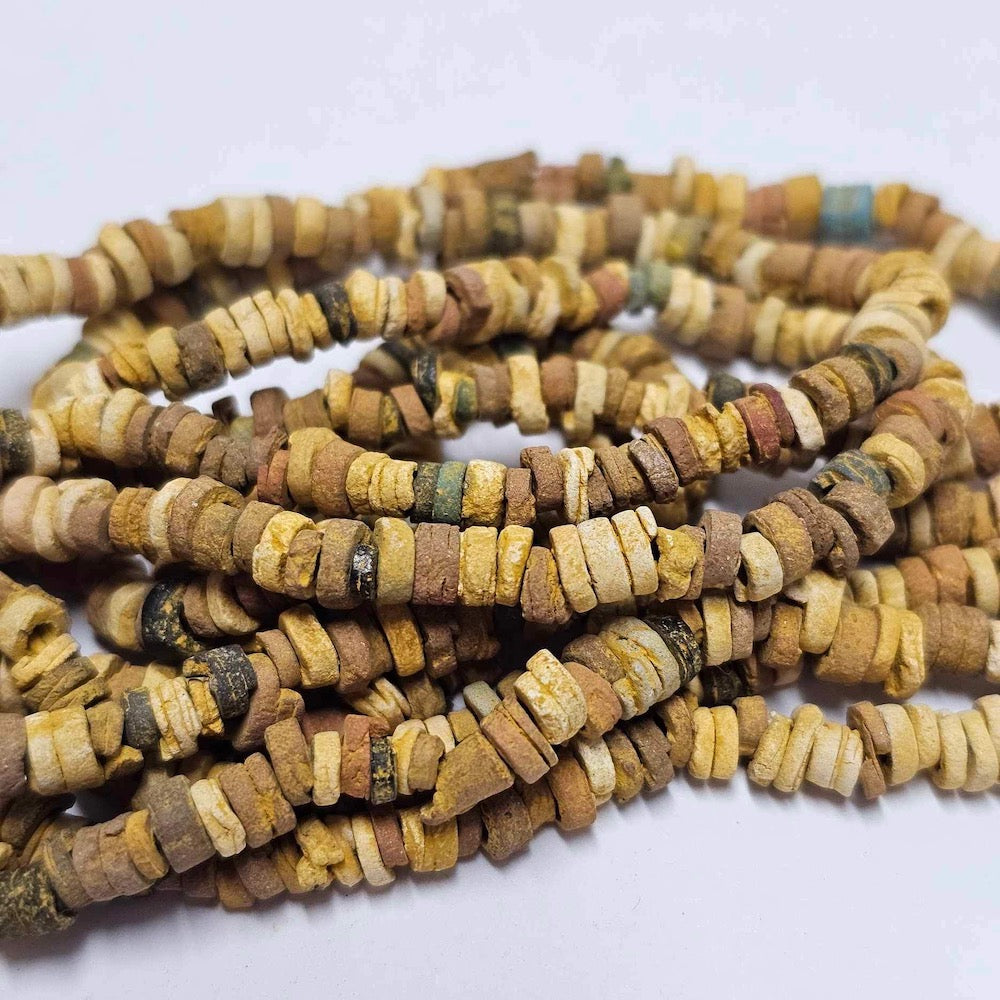 A collection of sand colored vintage faience beads arranged in lines, with varying shapes and textures.
